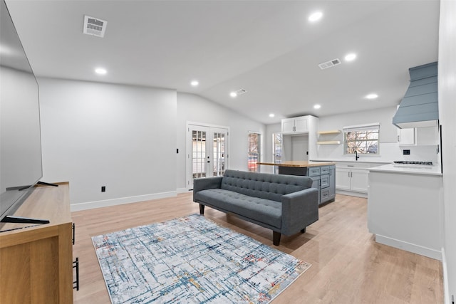 living room featuring light hardwood / wood-style floors, french doors, lofted ceiling, and sink