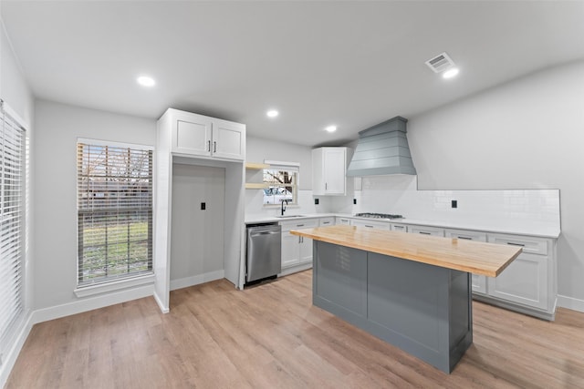 kitchen with white cabinets, custom exhaust hood, stainless steel appliances, and butcher block counters