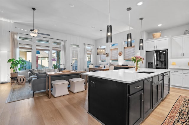 kitchen with appliances with stainless steel finishes, an island with sink, white cabinets, decorative light fixtures, and light wood-type flooring