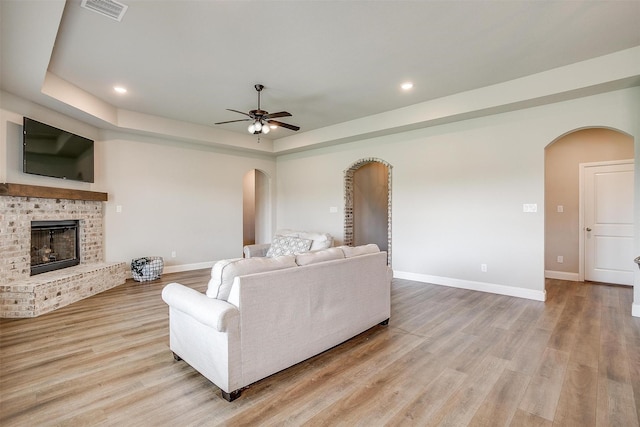 living room featuring a fireplace, light wood-type flooring, ceiling fan, and a tray ceiling