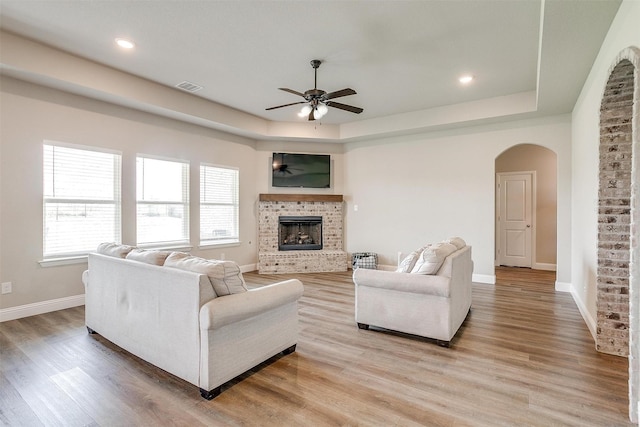 living room with a fireplace, a raised ceiling, ceiling fan, and light hardwood / wood-style floors