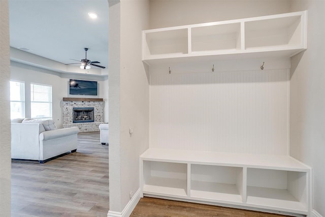 mudroom featuring wood-type flooring, a brick fireplace, and ceiling fan