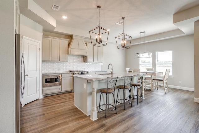 kitchen with decorative light fixtures, an island with sink, custom range hood, a tray ceiling, and a breakfast bar area