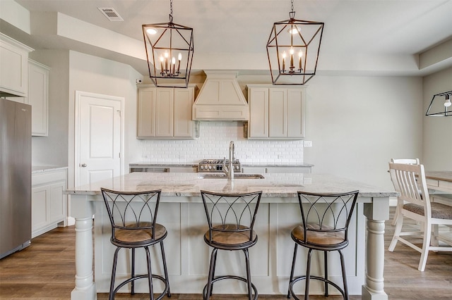 kitchen featuring sink, decorative light fixtures, a center island with sink, and stainless steel refrigerator