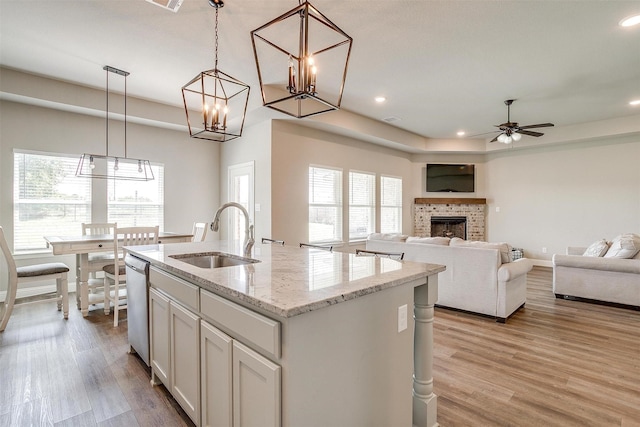 kitchen featuring an island with sink, light stone countertops, pendant lighting, a brick fireplace, and sink