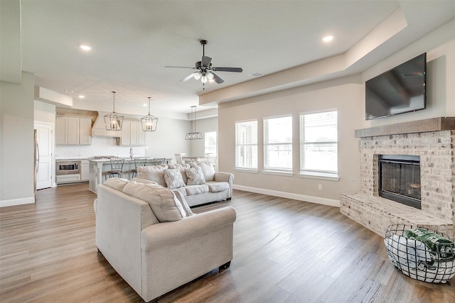 living room with a brick fireplace, ceiling fan, and light hardwood / wood-style floors