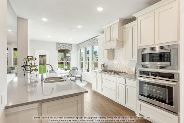 kitchen with light hardwood / wood-style flooring, stainless steel appliances, a kitchen island with sink, backsplash, and sink