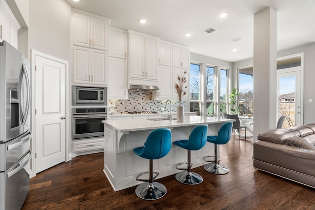 kitchen featuring white cabinets, a center island with sink, dark hardwood / wood-style flooring, exhaust hood, and appliances with stainless steel finishes