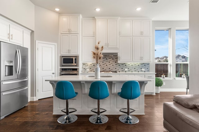 kitchen with tasteful backsplash, a kitchen island with sink, dark hardwood / wood-style flooring, white cabinets, and appliances with stainless steel finishes