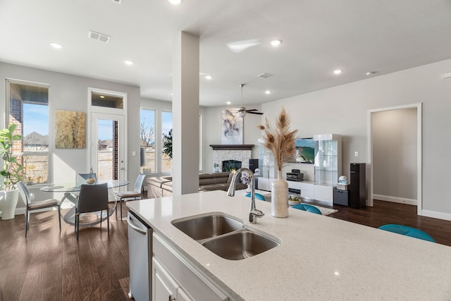 kitchen with sink, white cabinets, a fireplace, light stone counters, and stainless steel dishwasher