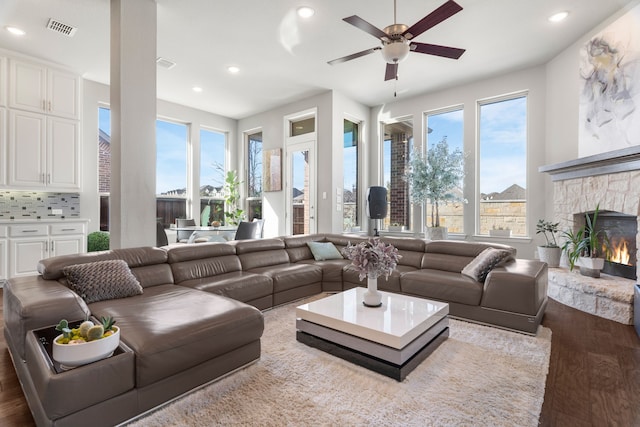 living room featuring ceiling fan, light hardwood / wood-style floors, and a stone fireplace