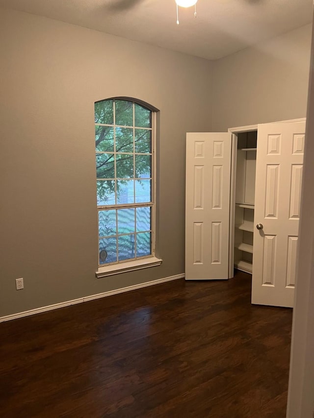 unfurnished bedroom with ceiling fan, a closet, multiple windows, and dark hardwood / wood-style floors