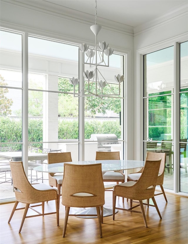 dining room featuring a healthy amount of sunlight, wood-type flooring, crown molding, and a chandelier