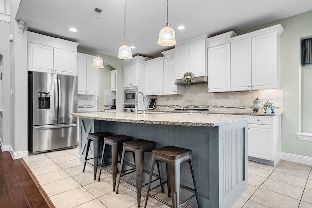 kitchen with white cabinets, appliances with stainless steel finishes, light tile patterned flooring, and a kitchen island with sink