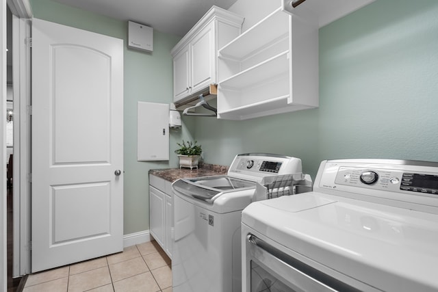 laundry room featuring washing machine and clothes dryer, light tile patterned floors, and cabinets