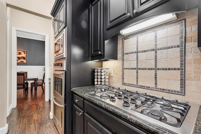 kitchen featuring stainless steel appliances, dark stone countertops, backsplash, and dark hardwood / wood-style flooring