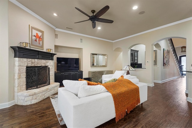 living room with ceiling fan, dark hardwood / wood-style floors, ornamental molding, and a stone fireplace