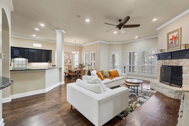 living room with a fireplace, dark hardwood / wood-style flooring, ceiling fan with notable chandelier, and ornamental molding