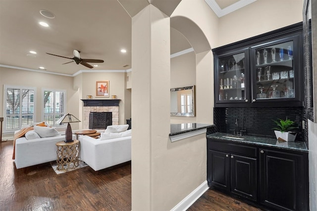 living room featuring a fireplace, ceiling fan, dark hardwood / wood-style floors, ornamental molding, and wet bar