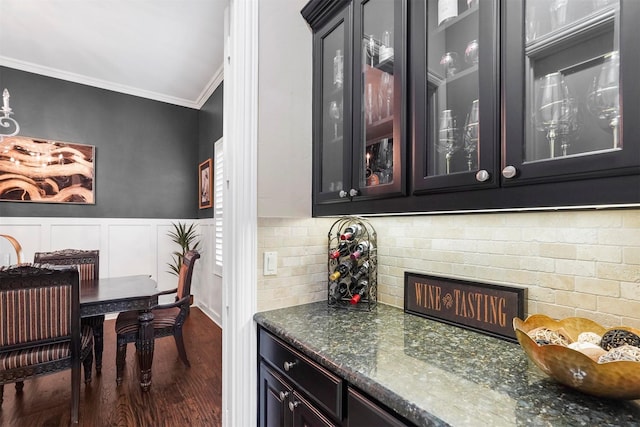 bar with dark hardwood / wood-style floors, ornamental molding, and dark stone counters