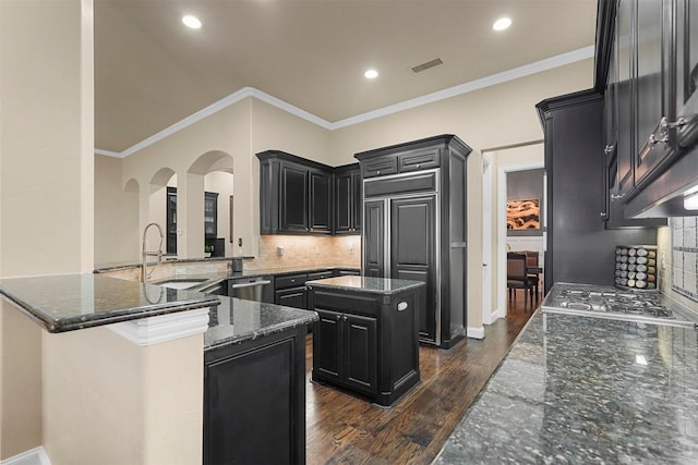 kitchen with a kitchen island, dark stone countertops, ornamental molding, and sink