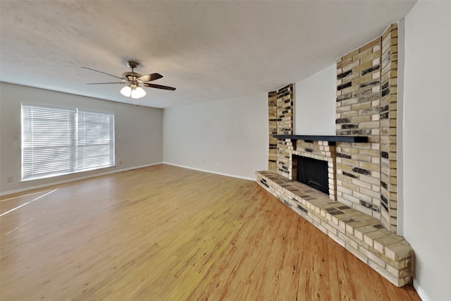 unfurnished living room featuring ceiling fan, a brick fireplace, and wood-type flooring