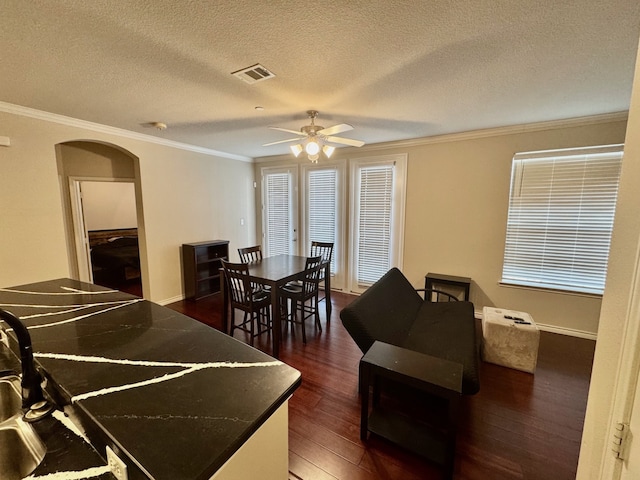 dining space featuring sink, a textured ceiling, ceiling fan, crown molding, and dark wood-type flooring