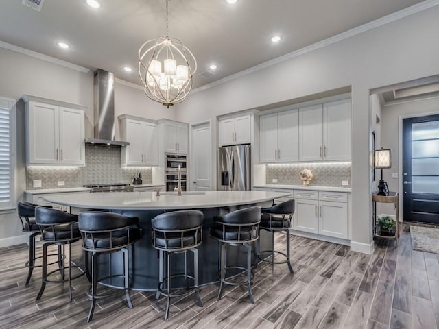 kitchen featuring a large island, stainless steel appliances, white cabinetry, and wall chimney range hood