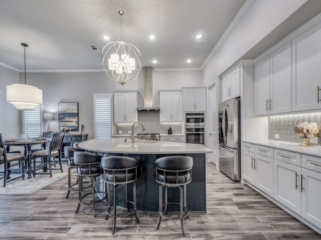 kitchen featuring stainless steel appliances, a center island with sink, ornamental molding, and hanging light fixtures