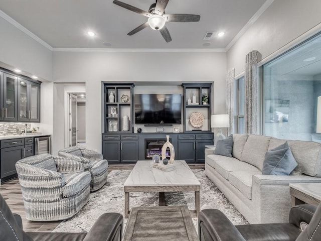 living room with light wood-type flooring, ceiling fan, crown molding, and wet bar