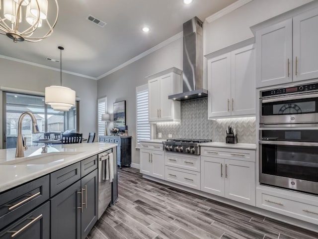 kitchen with stainless steel appliances, sink, white cabinets, wall chimney range hood, and pendant lighting