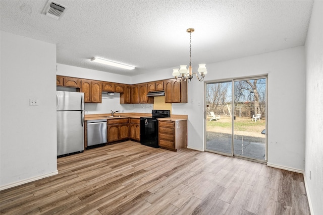 kitchen with stainless steel appliances, a notable chandelier, a textured ceiling, light hardwood / wood-style flooring, and decorative light fixtures