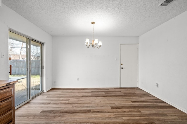 spare room featuring a textured ceiling, a notable chandelier, and light hardwood / wood-style flooring