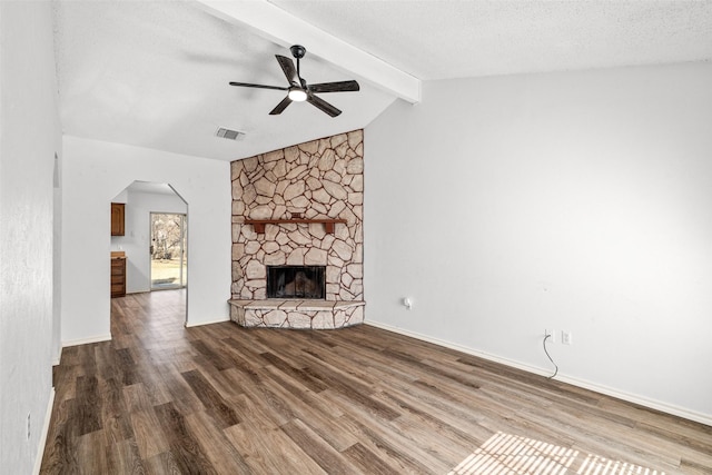 unfurnished living room with a textured ceiling, vaulted ceiling with beams, ceiling fan, hardwood / wood-style flooring, and a stone fireplace