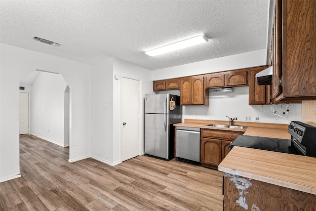 kitchen featuring stainless steel appliances, a textured ceiling, wall chimney exhaust hood, and sink