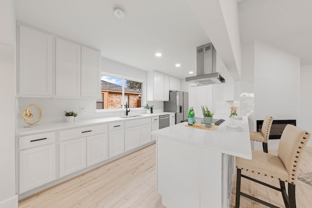 kitchen featuring island range hood, a breakfast bar area, appliances with stainless steel finishes, white cabinets, and sink