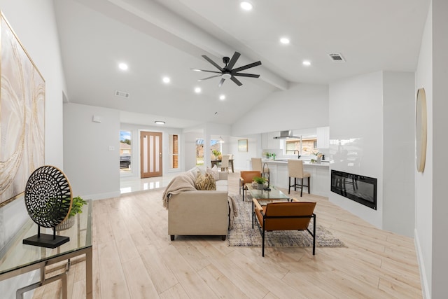 living room with beam ceiling, ceiling fan, light wood-type flooring, and high vaulted ceiling