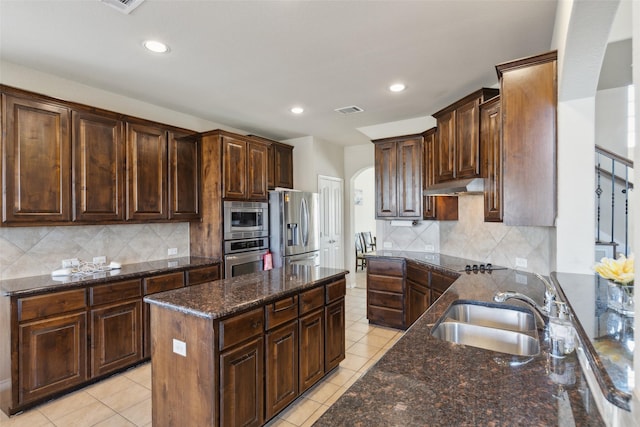 kitchen featuring stainless steel appliances, a center island, dark stone countertops, and sink