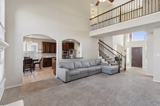 living room featuring a towering ceiling, ceiling fan, and light carpet