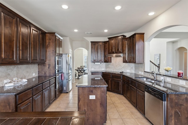 kitchen with stainless steel appliances, a kitchen island, dark stone counters, and dark brown cabinets