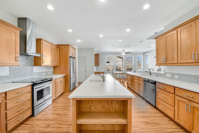 kitchen with sink, appliances with stainless steel finishes, light hardwood / wood-style floors, a center island with sink, and wall chimney exhaust hood