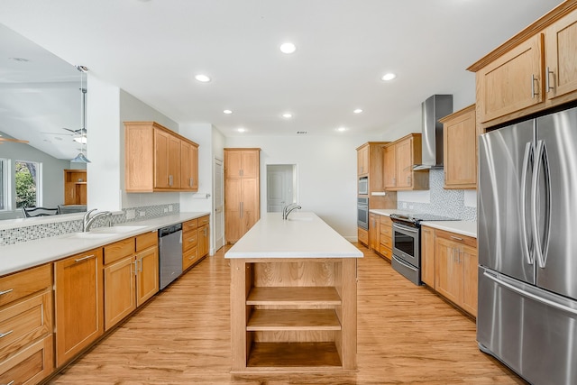 kitchen featuring sink, a kitchen island with sink, ceiling fan, stainless steel appliances, and wall chimney range hood