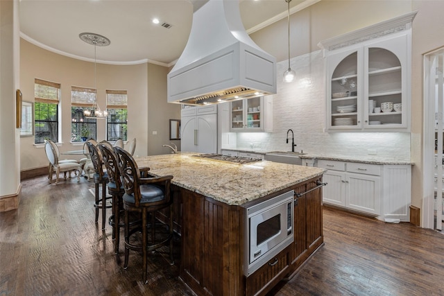 kitchen with an island with sink, built in appliances, premium range hood, sink, and white cabinetry