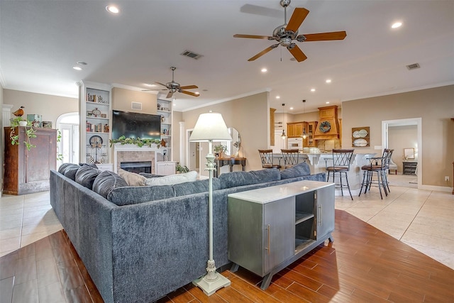 living room featuring a tile fireplace, ceiling fan, tile patterned floors, and ornamental molding