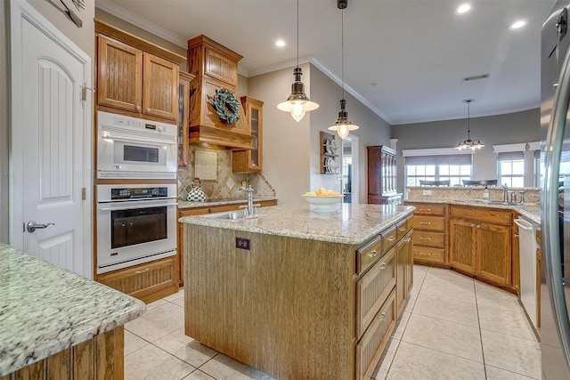 kitchen featuring appliances with stainless steel finishes, an island with sink, light stone counters, decorative light fixtures, and backsplash