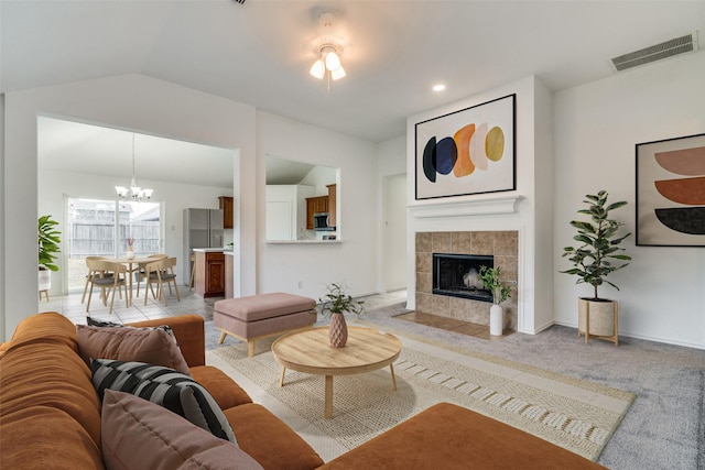 living room featuring an inviting chandelier, lofted ceiling, light colored carpet, and a tiled fireplace