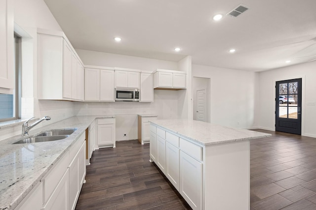 kitchen with a kitchen island, tasteful backsplash, sink, white cabinets, and light stone countertops