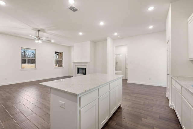 kitchen with white cabinetry, dark hardwood / wood-style flooring, a center island, ceiling fan, and light stone countertops