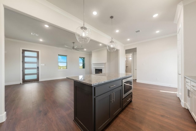 kitchen featuring light stone counters, dark wood-type flooring, stainless steel microwave, decorative light fixtures, and white cabinets