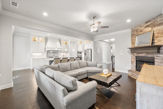 living room with ceiling fan, a fireplace, crown molding, and dark wood-type flooring